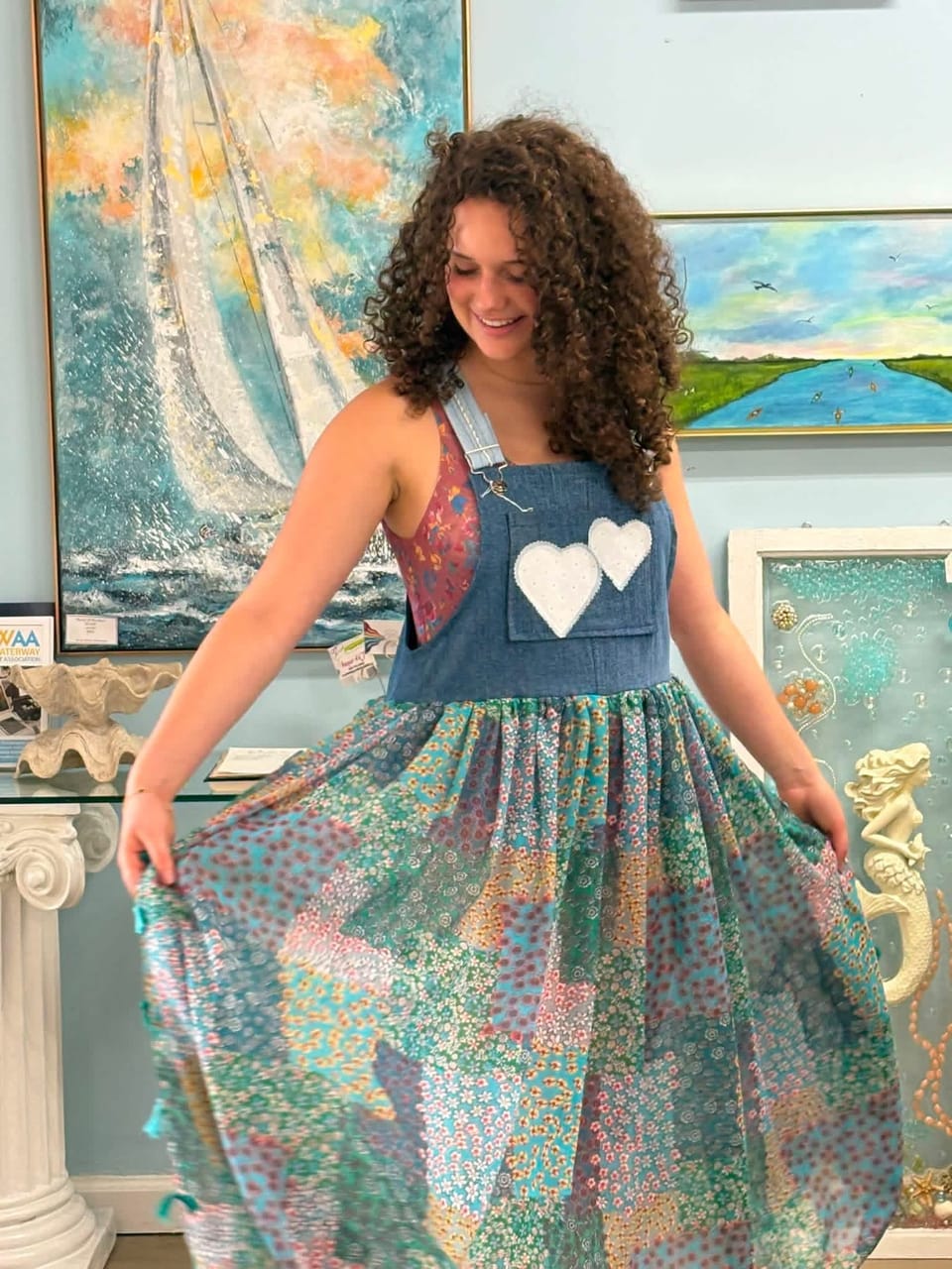 Young woman twirling a patchwork dress with heart pockets in the gallery