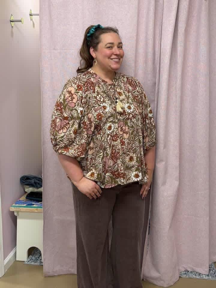 Smiling woman in a floral peasant blouse and wide-leg pants in the fitting room
