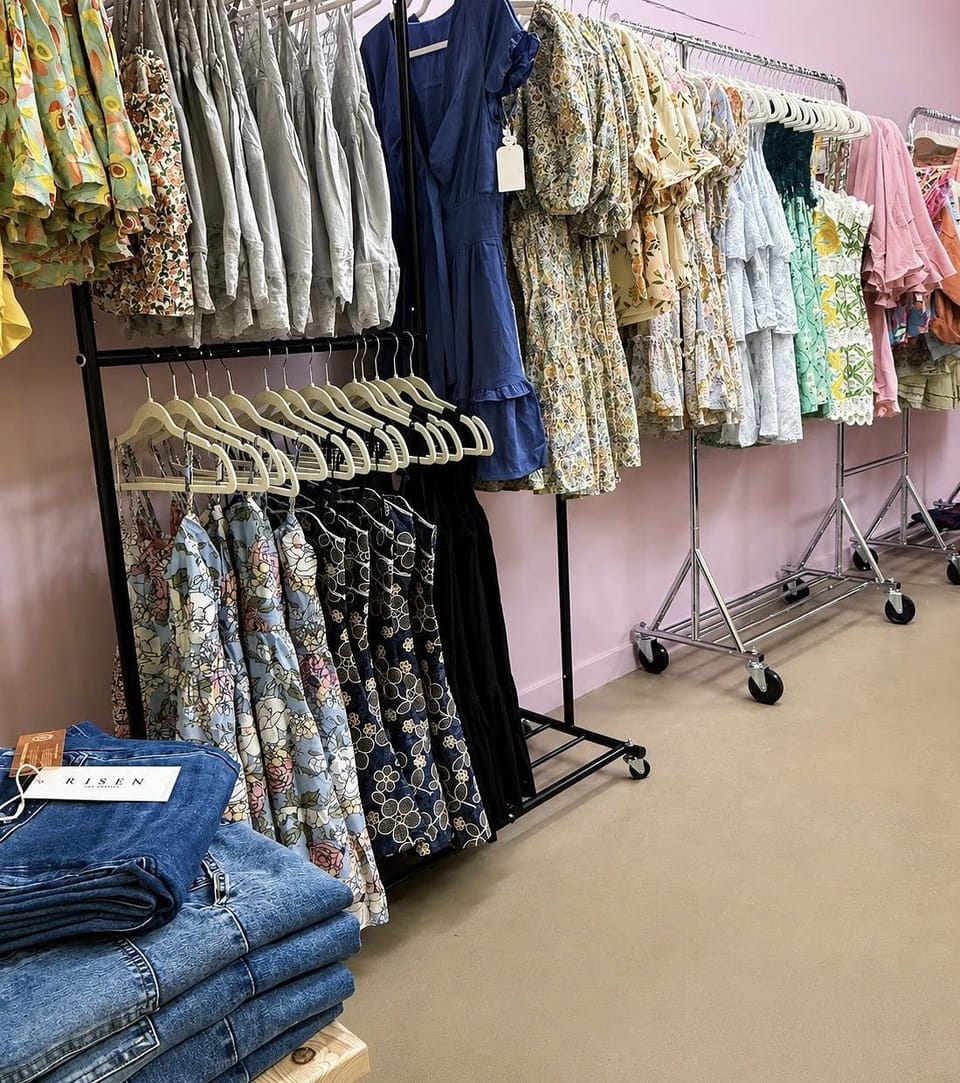 Racks of new floral dresses and Risen jeans against a pink boutique wall